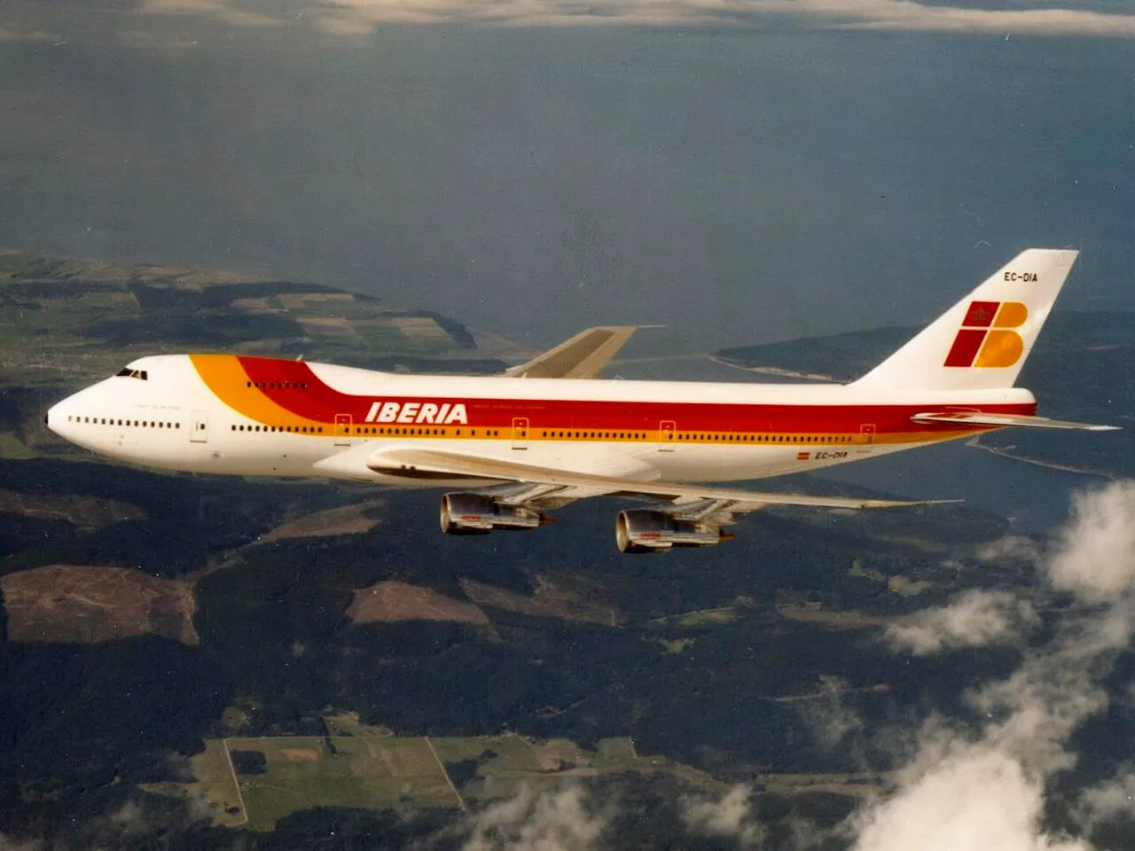 An Iberia Boeing 747-200 in flight against a blue sky with clouds.